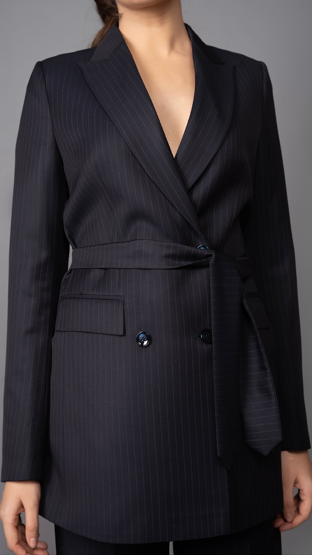 A close-up of the belted waist on the blue pinstripe blazer, highlighting its structured fit and modern tailoring.