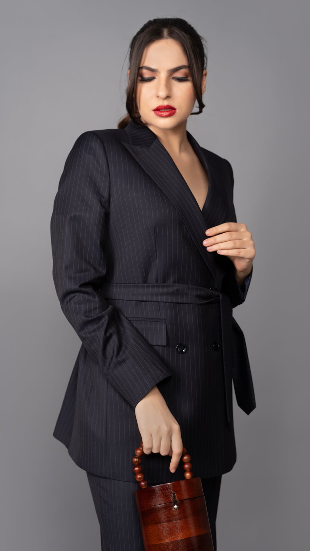 A contemporary blue pinstriped blazer, featuring a classic peak lapel and a waist-cinching belt, redefining modern formalwear.