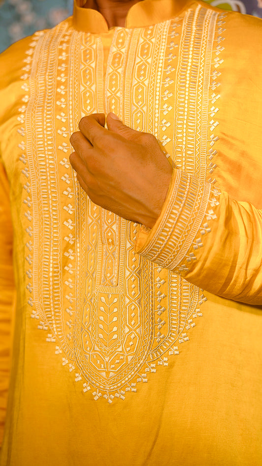 Close-up of a mustard embroidered garment with a hand touching the fabric.