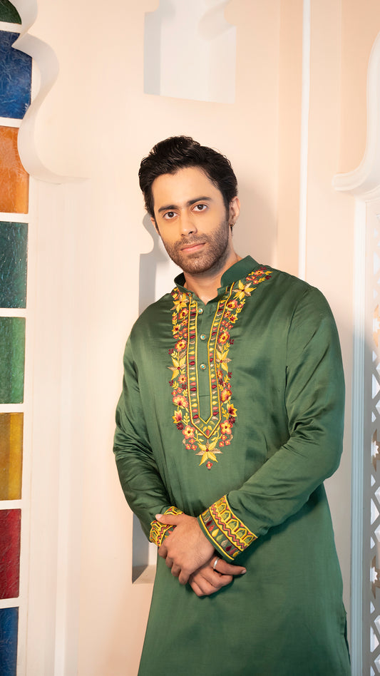 Man wearing a green embroidered traditional outfit standing indoors.