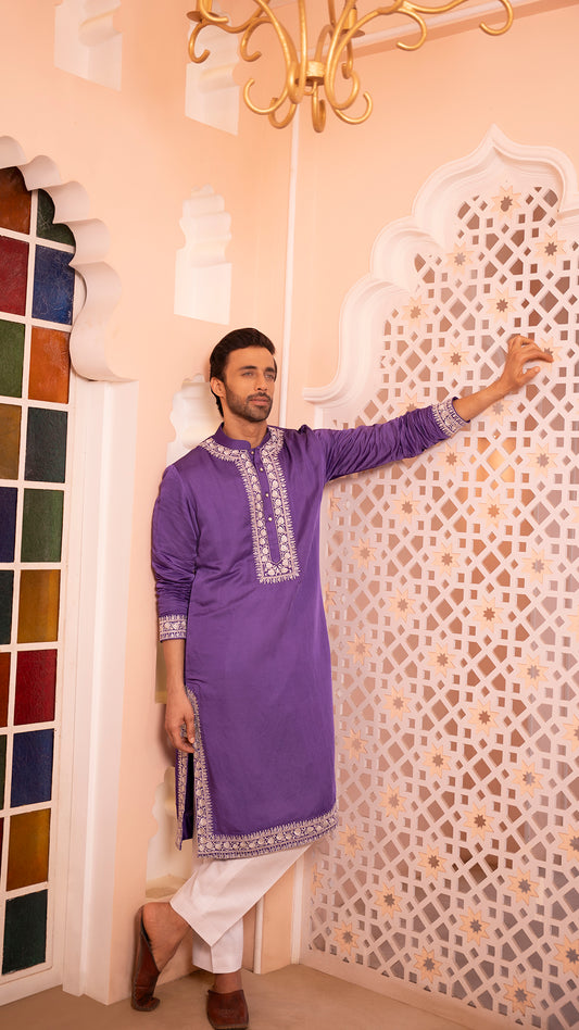 Man wearing a purple kurta with white pants in a decorated room.