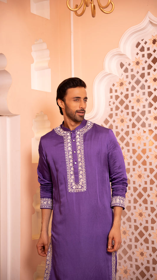 Man wearing a purple embroidered kurta against an ornate wall.