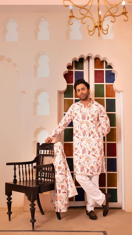 Man in a floral kurta standing in a room with decorative wall and chandelier.