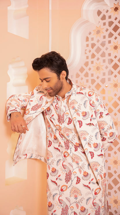 Man wearing a floral patterned kurta jacket against an ornate wall.