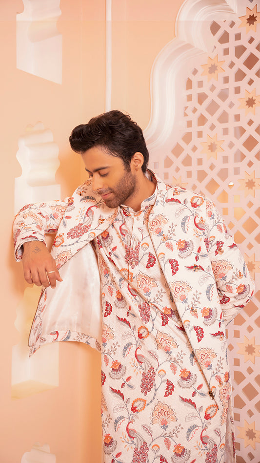 Man wearing a floral patterned kurta jacket against an ornate wall.