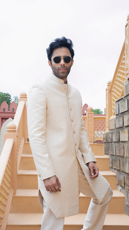 Man wearing a cream sherwani with sunglasses on a staircase background