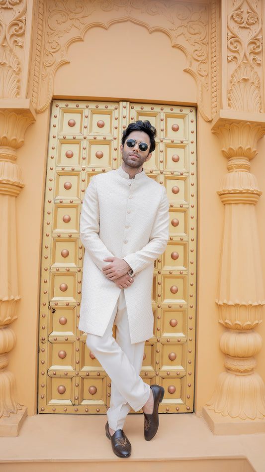 Man in a white traditional outfit standing in front of an ornate golden door.