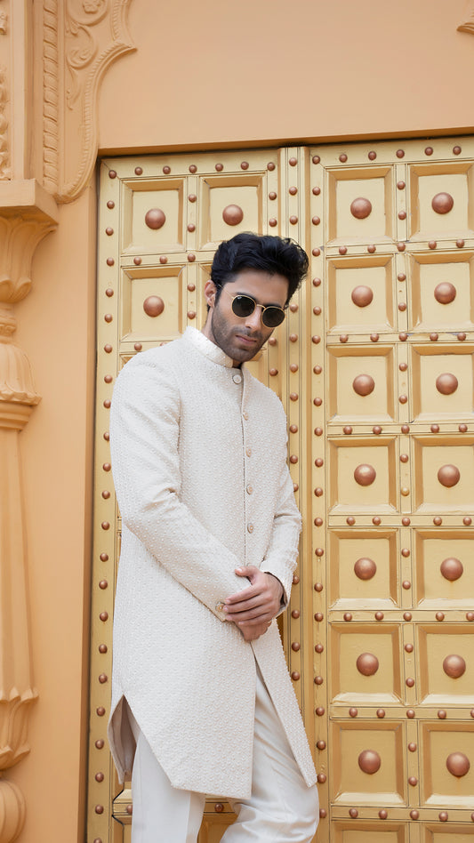 Man in a white traditional outfit standing in front of a decorative door.