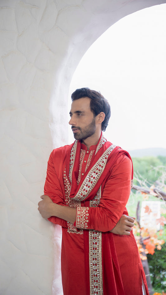 Man wearing a red Kurta with white patiala against a blurred outdoor background