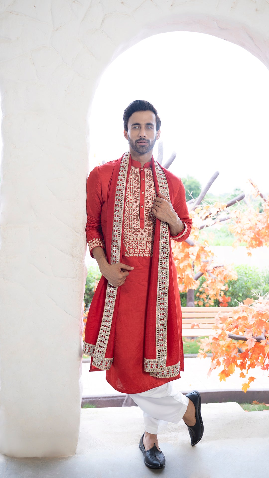 Man wearing a red Kurta with white patiala and red stole standing in a bright outdoor setting.