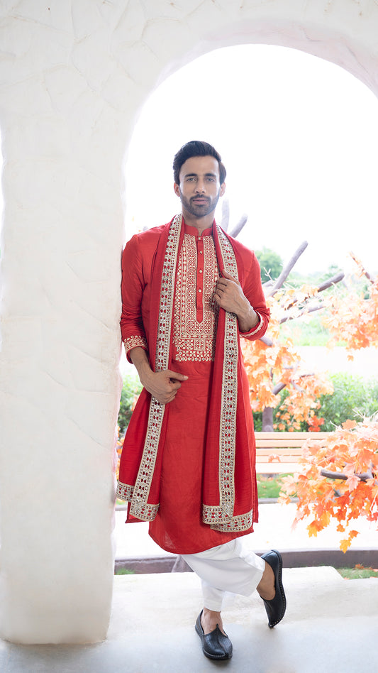 Man wearing a red Kurta with white patiala and red stole standing in a bright outdoor setting.