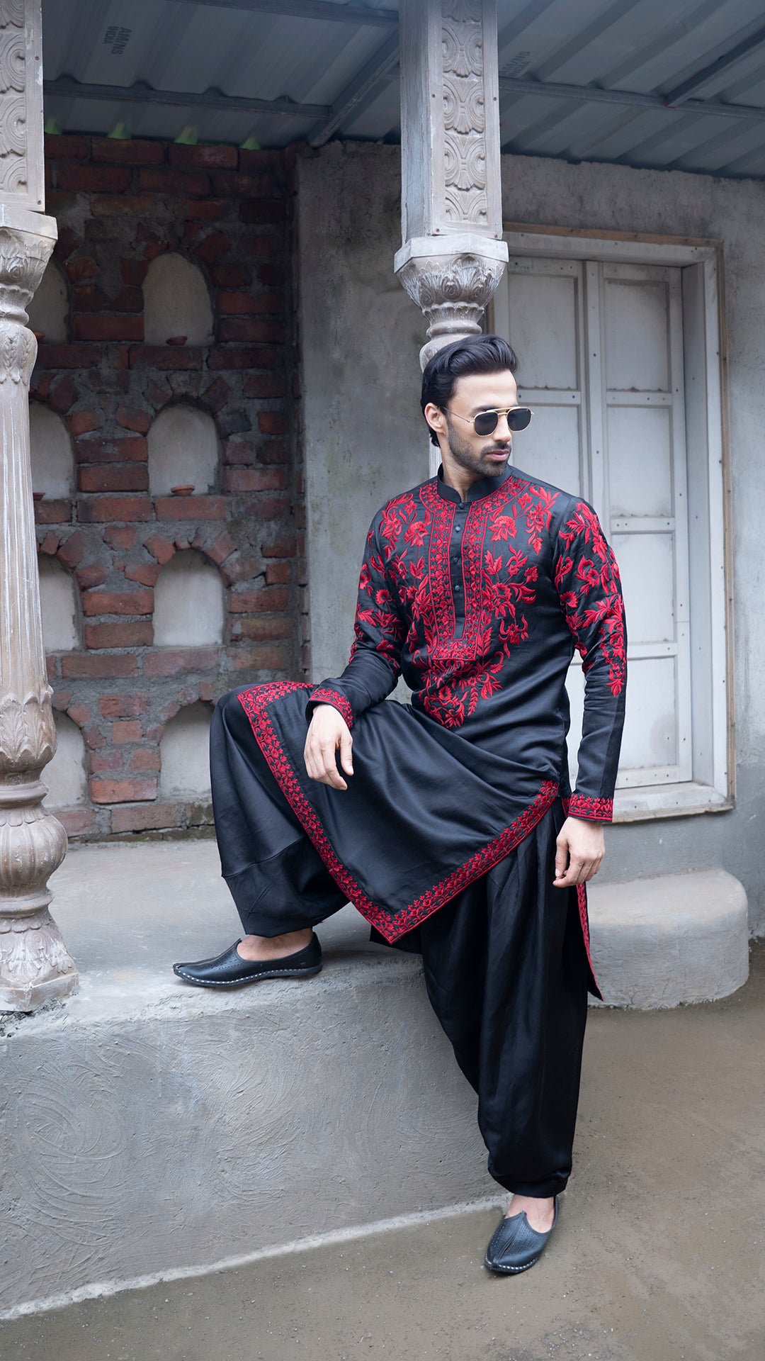 Man in traditional black and red outfit sitting on a stone step.