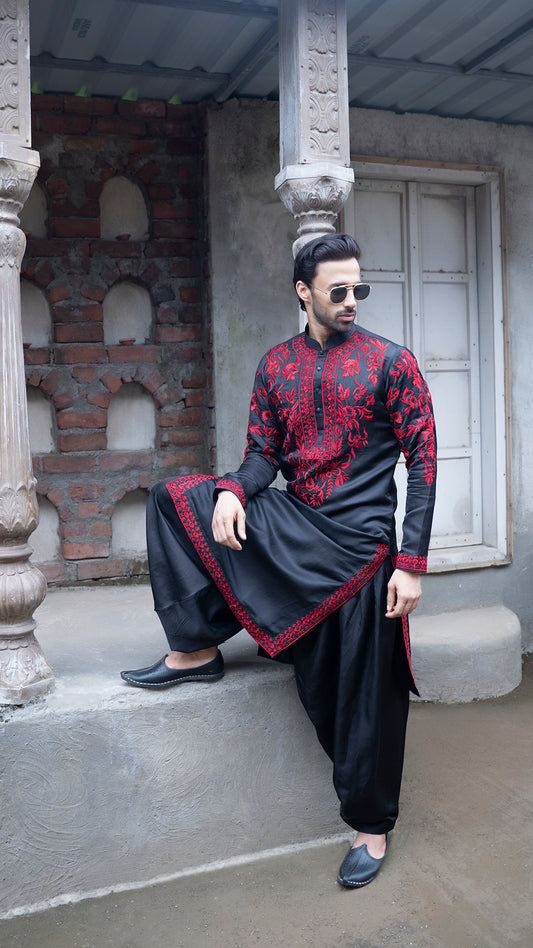 Man in traditional black and red outfit sitting on a stone step.