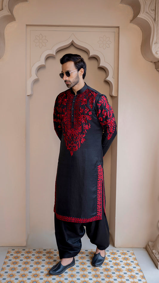 Man wearing a black kurta with red embroidery standing in front of an archway.