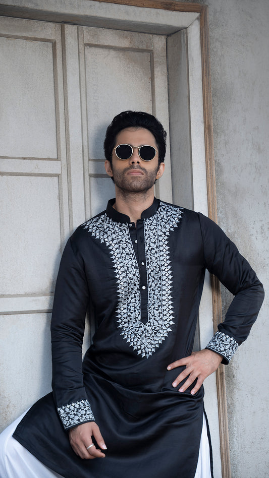 Man wearing a black embroidered kurta with grey patterns against a neutral background