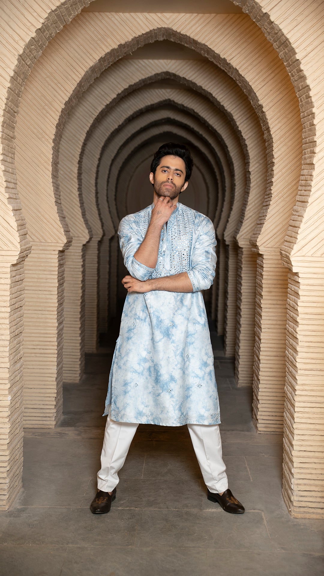Man in a blue tye-dye kurta standing in a architectural archway.