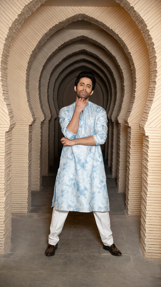 Man in a blue tye-dye kurta standing in a architectural archway.