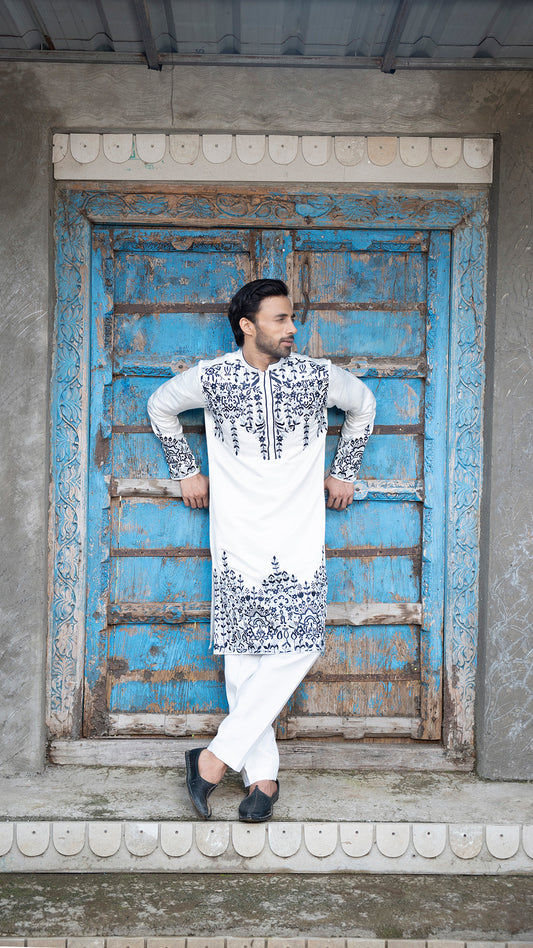Man wearing a traditional outfit standing in front of a blue door.