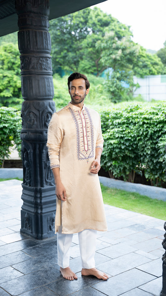 Man wearing a beige kurta with white pants standing outdoors on a stone path.