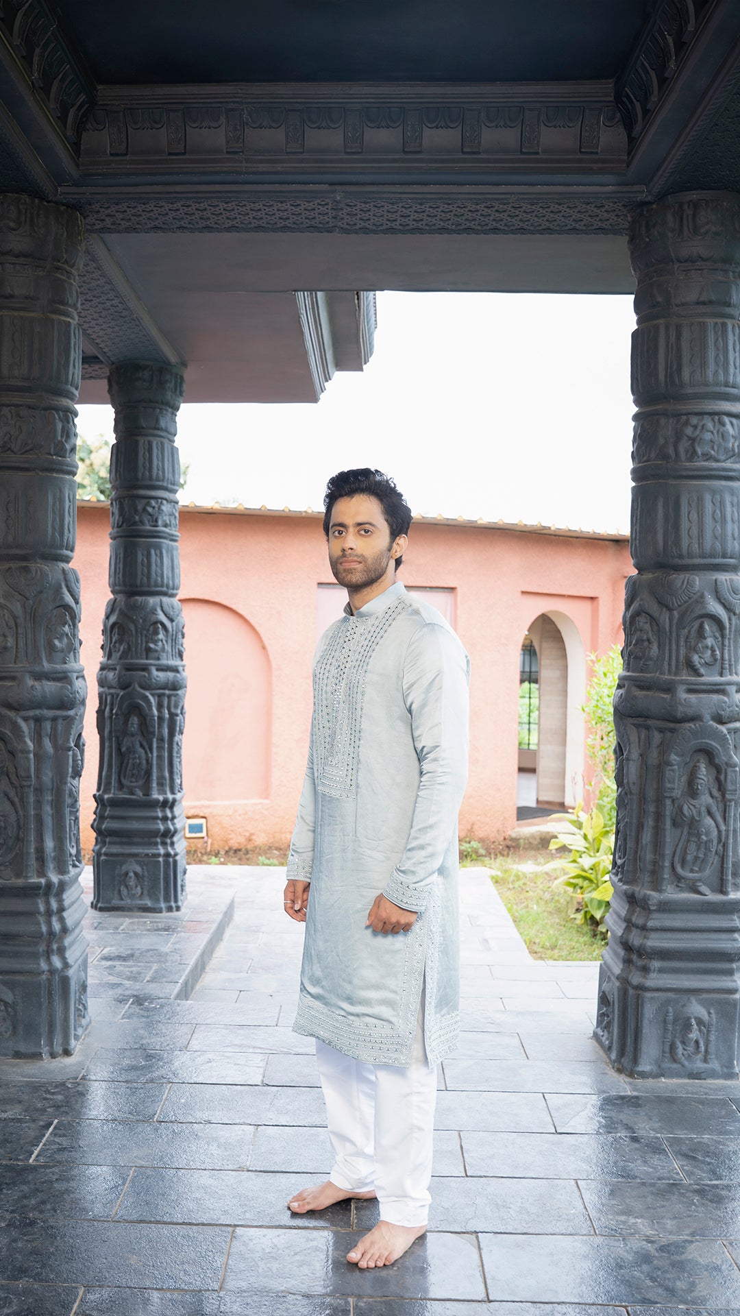 Man in traditional attire standing under a stone archway with a temple-like background