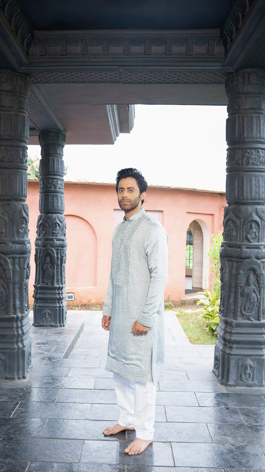 Man in traditional attire standing under a stone archway with a temple-like background