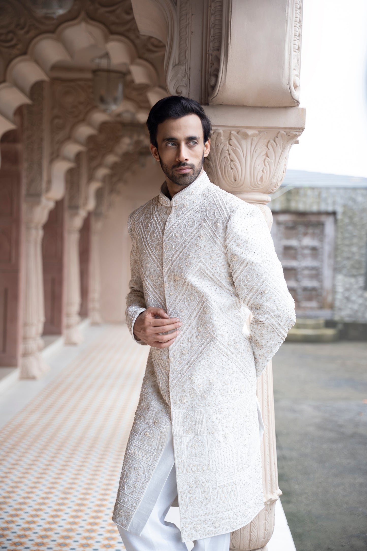 Man wearing a traditional white sherwani in an architectural setting