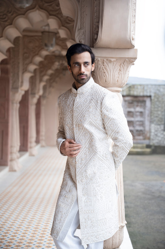 Man wearing a traditional white sherwani in an architectural setting