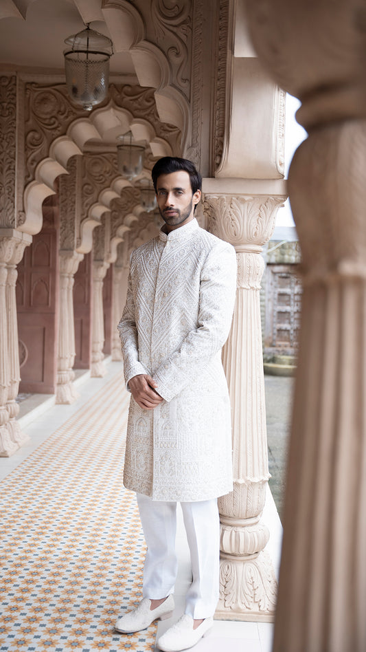 Man in a traditional white sherwani standing in an ornate architectural setting