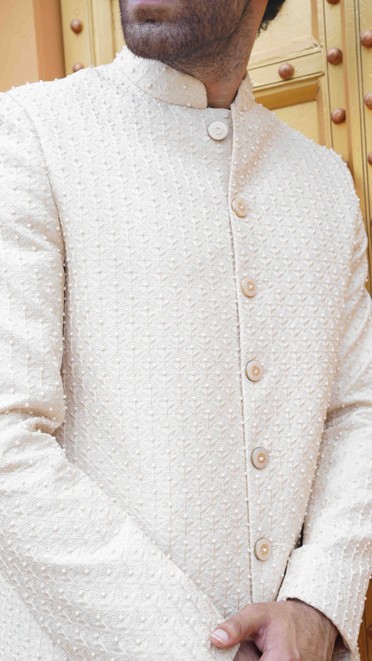Close-up of a person wearing a cream-colored traditional jacket with buttons.