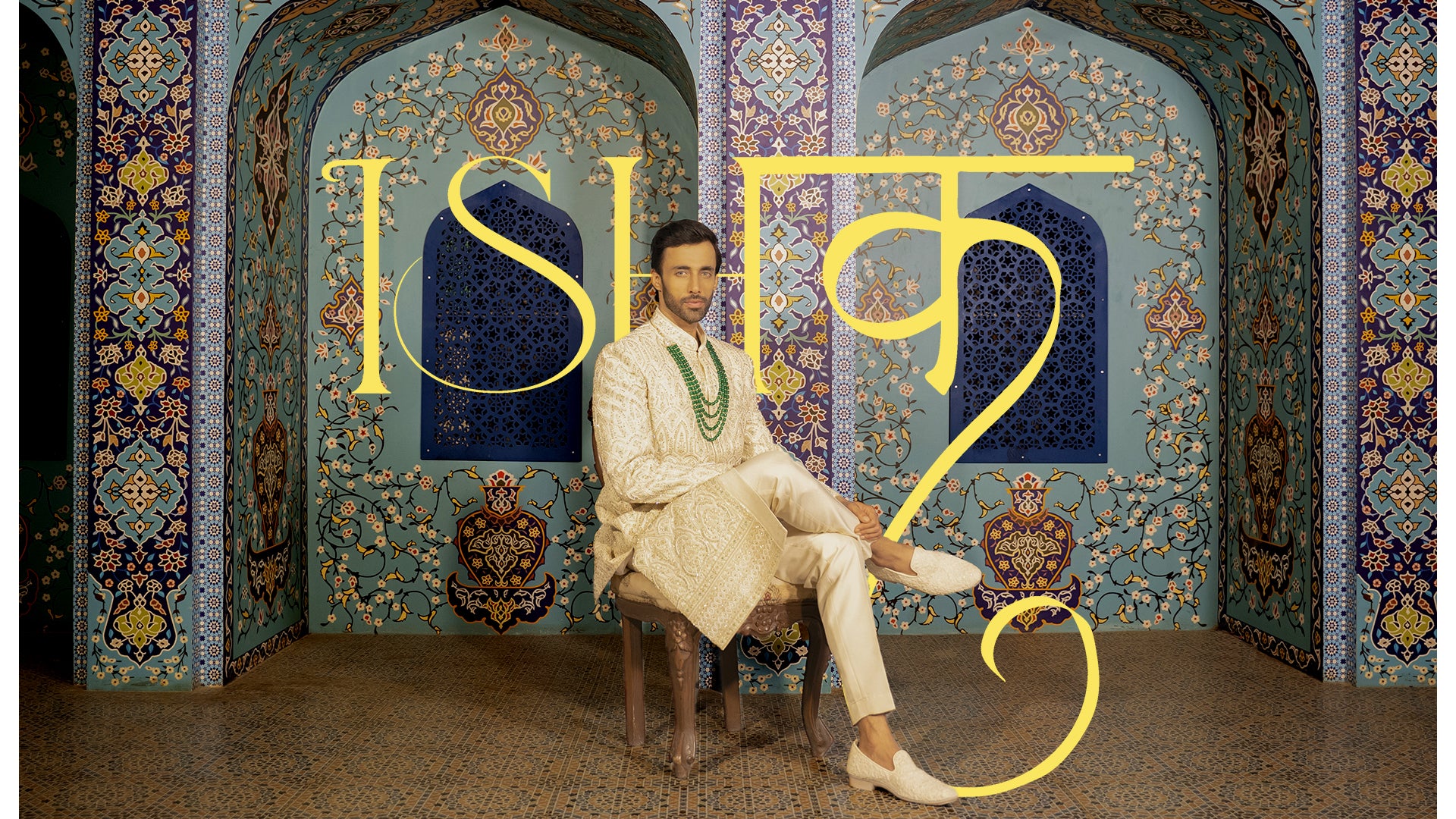 Man sitting in a ornate room with decorative walls and 'Ishq' text.
